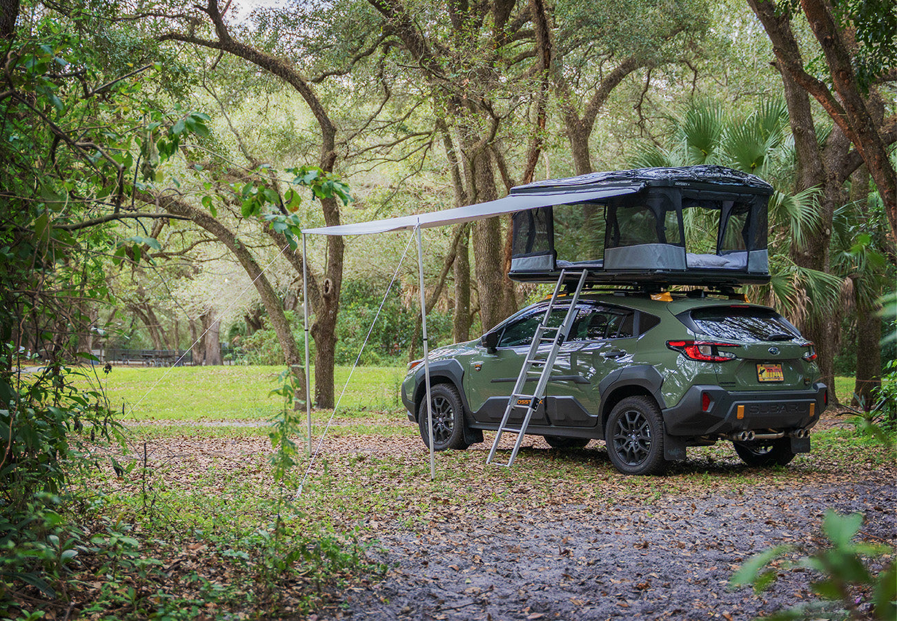 Green SUV with a rooftop tent parked in a forested area